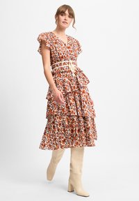 Blumenkleid mit rüschierten Ärmeln, gestuftem Design, orange-blauen Mustern, tailliert mit einem beigen Gürtel, kombiniert mit knielangen beigen Stiefeln.