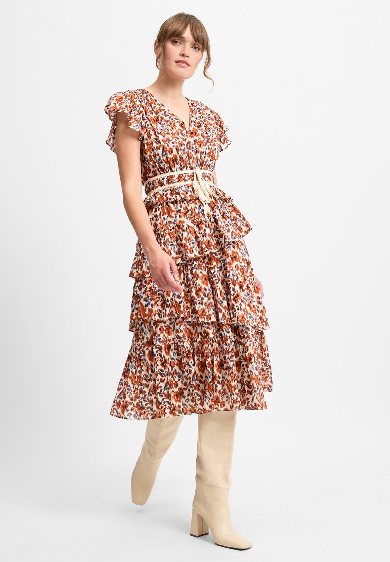Blumenkleid mit rüschierten Ärmeln, gestuftem Design, orange-blauen Mustern, tailliert mit einem beigen Gürtel, kombiniert mit knielangen beigen Stiefeln.