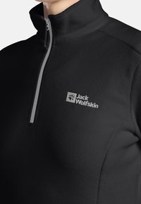 Czarny polarowy pulower z wysokim kołnierzem i zamkiem na trzy czwarte. Szary zamek i subtelne wyszycie logo Jack Wolfskin na piersi.