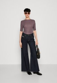 Úzký mauve body s krátkým rukávem spárovaný s širokými tmavými džíny. Modelka drží černou kabelku a nosí velké sluneční brýle.