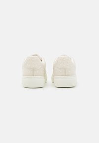 Sneaker beige con una toma superiore testurizzata decorata con strass trasparenti, punta arrotondata e suola in gomma bianca solida.