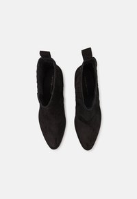 Botas negras hasta el tobillo, hechas de suave ante, con punta afilada y acentos de costillas verticales, con tiradores para ponerlas fácilmente.