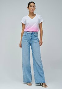 Camiseta blanca de cuello en V con ombre rosa, combinada con jeans de pierna ancha de talle alto en azul claro y sandalias de tacón beige.