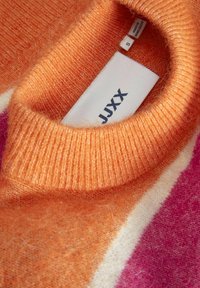 Pomarańczowy wełniany sweter z prążkowanym kołnierzem, z kolorowym wzorem w odcieniach pomarańczu, kremu i różu. Widoczna metka z instrukcją pielęgnacji.