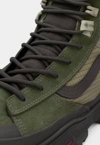 Green suede and fabric high-top sneaker featuring dark laces, a patterned side, and a prominent logo tag near the ankle. Rubber sole.