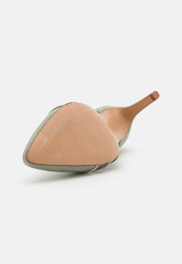 Chaussure à talon haut en suède vert avec un bout pointu, dotée d'une semelle lisse et texturée et d'accents décoratifs en strass le long du bord.