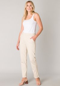 Beige op maat gemaakte broek met zijzakken, uitgerust met een knoop tailleband en een slim fit. Gekoeld met een eenvoudige witte tanktop en strappy hakken.