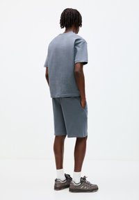T-shirt en coton gris à manches courtes et shorts assortis, avec une coupe décontractée et des poches latérales, associés à des baskets grises et des chaussettes blanches.