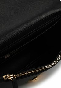 Schwarze Lederhandtasche mit strukturierter Oberfläche, einem Reißverschluss mit goldfarbenen Beschlägen und einem offenen Innenraum ohne sichtbare Fächer.