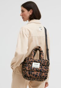 Braun-schwarze Tasche mit Leopardenmuster, gepolstertem Design, zwei Griffen, verstellbarem Riemen und einem Markenlabel auf der Vorderseite.
