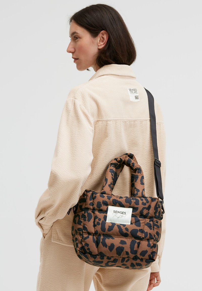 Braun-schwarze Tasche mit Leopardenmuster, gepolstertem Design, zwei Griffen, verstellbarem Riemen und einem Markenlabel auf der Vorderseite.