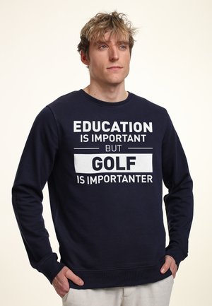 Námořnická modrá mikina s bílým textem "VZDĚLÁNÍ JE DŮLEŽITÉ, ALE GOLF JE DŮLEŽITĚJŠÍ." Má klasický kulatý výstřih a žebrované manžety.