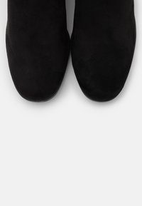 Svarta mockaskor i ankelhöjd med rund tå och platt sula, med en slät yta och en enkel, minimalistisk design.