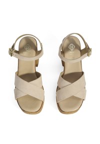 Sandales en suède beige avec des sangles croisées, une semelle rembourrée et un talon en liège de hauteur moyenne. Bride de cheville réglable avec boucle dorée.