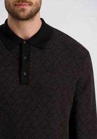Schwarzes Polohemd mit Muster, das ein strukturiertes Design, eine kurze Knopfleiste und einen einfarbigen schwarzen Kragen aufweist.