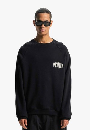 Black crewneck sweatshirt with long raglan sleeves, featuring a white printed logo on the chest and a textured fleece material.