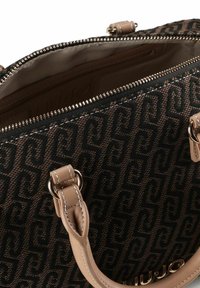 Borsa a mano marrone con motivo, esterno in tessuto strutturato, dettagli in pelle beige e chiusura con cerniera. Presenta doppi manici e elementi in metallo dorato.