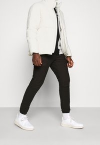 Chaqueta acolchada blanca con un alto cuello, combinada con pantalones ajustados negros y zapatillas blancas. El conjunto tiene un aspecto casual y en capas.