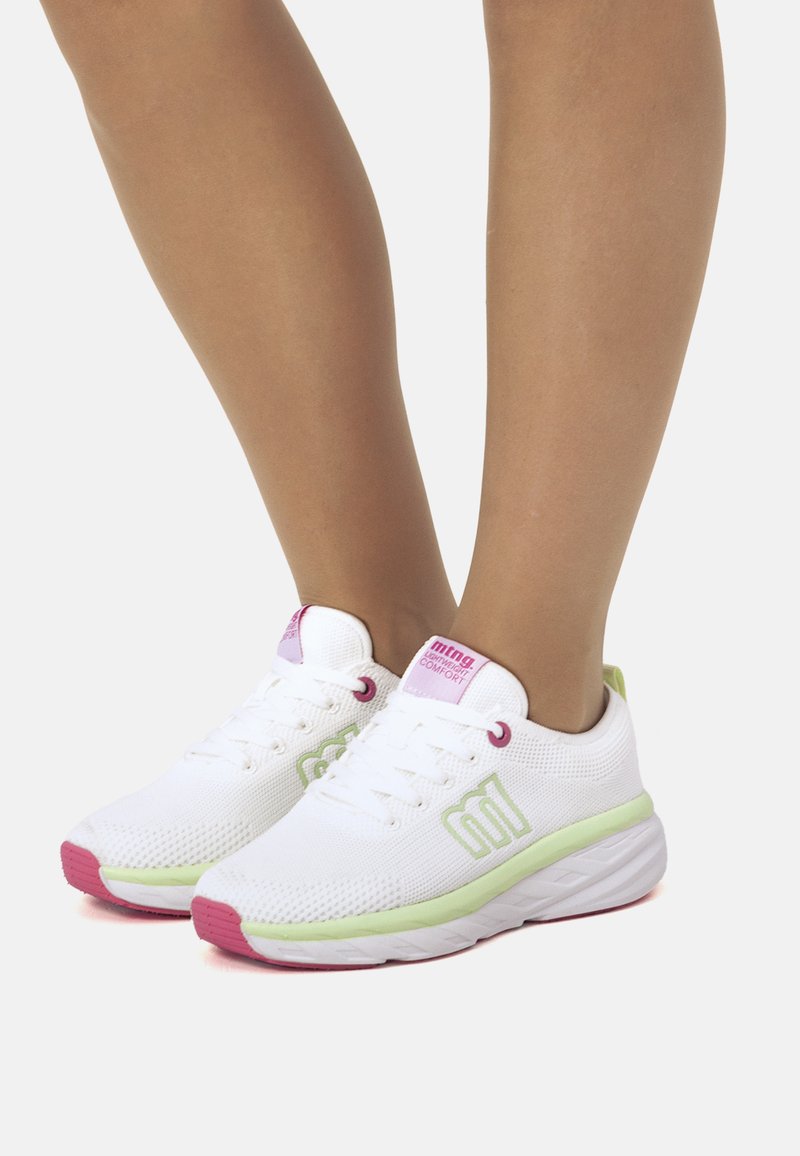 Zapatillas deportivas blancas con parte superior de malla, acentos verdes y suela rosa. Presentan cordones y una etiqueta de marca en la lengüeta.
