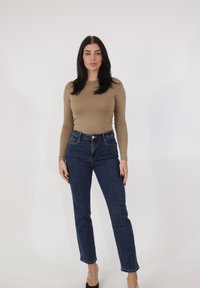 Top beige de manga larga combinado con vaqueros azul oscuro de talle alto. El conjunto presenta un diseño ajustado y una textura clásica de denim.