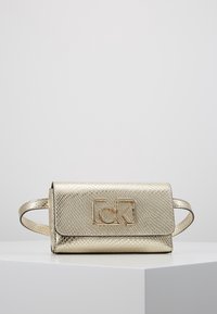 Kultainen teksturoitu clutch-laukku, jossa on käärmeennahkakuosi, ja jossa on läpän suljenta sekä näkyvä kultainen logo edessä. Kaksi kapeaa kahvaa.