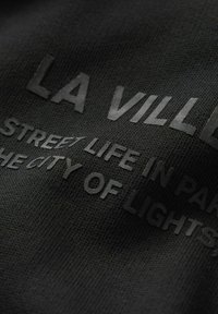 Musta tekstuur, millel on ülespoole ulatuvad, matt mustad tähed, mis ütlevad "LA VILLE" ja "STREET LIFE IN PARIS, THE CITY OF LIGHTS." Tekstuur on kootud.