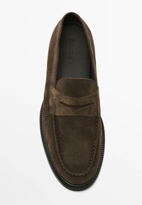 Brune ruskindsloafer med en glat tekstur, udstyret med en syet tåhætte og en dekorativ frontaccent. Sort gummisål, rund form.