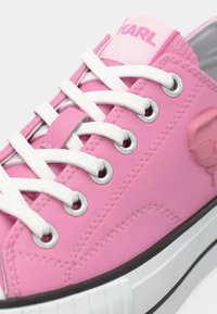 Ροζ αθλητικό παπούτσι με λείο καουτσούκ υλικό, λευκά κορδόνια, ασημένια μεταλλικά τρύπια και ροζ ταμπέλα με λογότυπο στη φτέρνα. Διαθέτει ανάγλυφη λεπτομέρεια λογότυπου στο πλάι.