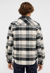 Kurtka koszulowa z polaru w czarno-kremową kratę. Posiada kołnierzyk i mankiety na guziki. Miękka w dotyku o luźnym kroju.