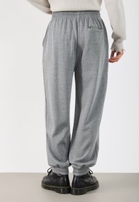 Grå, løstsittende sweatpants med strammet liv og mansjetter, med en baklomme. Brukes med svarte snøresko.