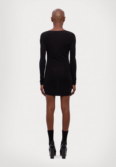 Black fitted dress with long sleeves, round neckline, and mini length. Worn with black ankle socks and glossy black high-heeled shoes.