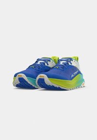 Baskets de course bleues avec des accents vert lime, tige en mesh texturé, semelle rembourrée et logo Vibram sur une semelle extérieure blanche.