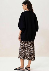 Un sweatshirt noir surdimensionné associé à une jupe midi à imprimé léopard, complété par des sandales plates noires. Tissu lisse, silhouette décontractée et motif unique.