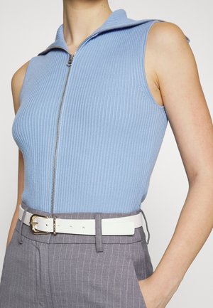Haut sans manches côtelé bleu clair zippé, porté avec un pantalon gris à rayures taille haute et une ceinture blanche avec boucle dorée.