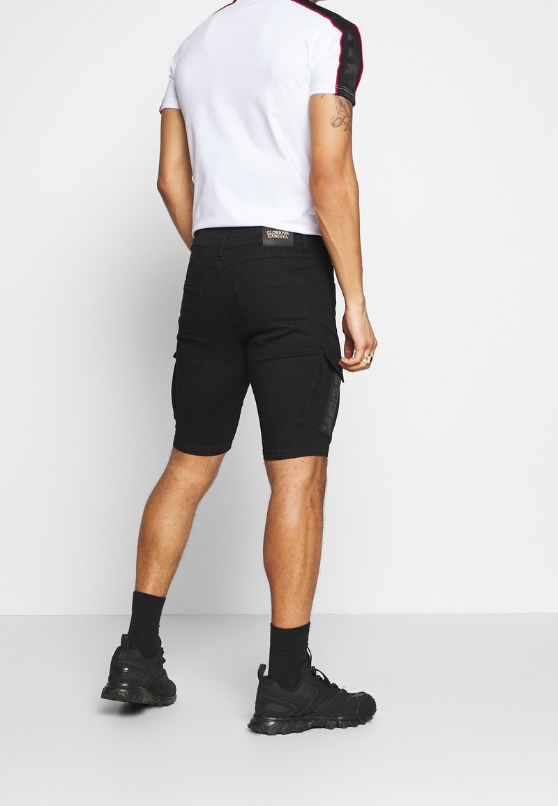 Shorts cargo noirs à coupe slim, avec poches latérales et un subtil détail de logo, associés à un t-shirt blanc et des baskets noires.