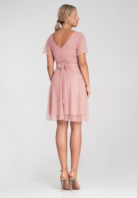 Różowa sukienka z krótkimi prześwitującymi rękawami, V-kształtnym dekoltem z tyłu oraz związanym w talii pasem, z luźną spódnicą sięgającą do połowy uda. Noszona z sandałami na obcasie.