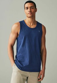Mørkeblå ærmeløs tanktop i blød bomuld med rund halsudskæring og et lille logo på brystet, parret med let beige shorts.