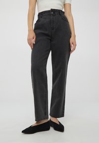 Czarne dżinsy o wysokim stanie z fakturowanym wykończeniem, prostą nogawką i elastycznym pasem, połączone z czarnymi płaskimi butami.