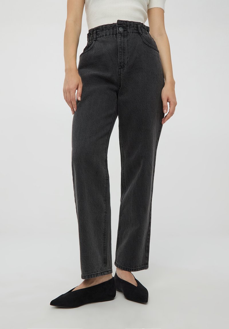 Czarne dżinsy o wysokim stanie z fakturowanym wykończeniem, prostą nogawką i elastycznym pasem, połączone z czarnymi płaskimi butami.