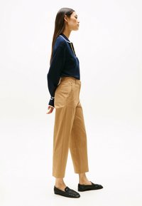 Polo en maille marine avec un col blanc, associé à un pantalon taille haute beige et des mocassins noirs. La tenue présente une coupe décontractée.