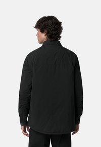 Giacca nera, leggera, con una vestibilità rilassata, maniche lunghe e colletto con bottoni. Presenta una texture liscia e un design semplice.