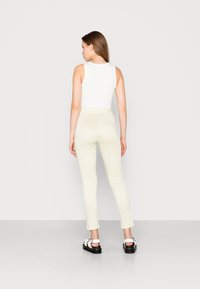 Top branco sem mangas combinado com calças xadrez amarelas claras, de design ajustado e comprimento até o tornozelo, complementado por sandálias pretas.