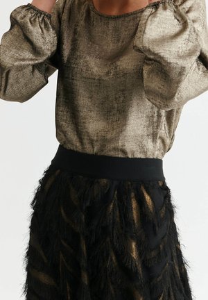 Haut métallisé doré à manches longues avec une finition texturée, associé à une jupe noire présentant une frange en couches ressemblant à des plumes et une taille solide.