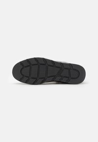Suela de zapato de goma negra con un patrón de textura, que presenta estrías y un logotipo embosado en el centro. Acabado de borde liso.