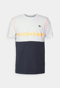 Lacoste-t-shirt med rund halsringning, korta ärmar, har vita, marinblå och orange färgblock, texturerad tyg och en logotyp på bröstet.