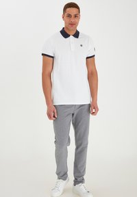 Hvid polo shirt med marineblå krave og ærme trim, tre-knaps placket, parret med lysegrå bukser og hvide sneakers.