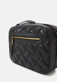 Črna usnjena torba z woven teksturo, ki ima sprednjo žeppo z zlatim zadrgo in ročajem na vrhu. Pravokotna oblika, minimalističen dizajn.