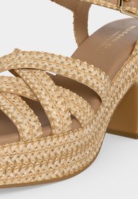Μπεζ υφαστένια πλατφόρμα πέδιλο με χοντρό τακούνι, τρεις μπροστινούς ιμάντες και πόρπη αστραγάλου.