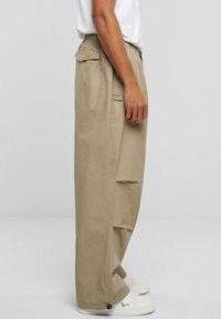 Pantalons cargo larges beiges avec une taille élastique, des poches latérales et une texture lisse, associés à des baskets blanches.