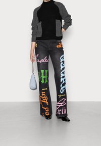 Svarta jeans med färggrafiska texter i rosa, orange, blått och grönt. Kombinerat med en svart och grå texturerad tröja och en liten blå väska.